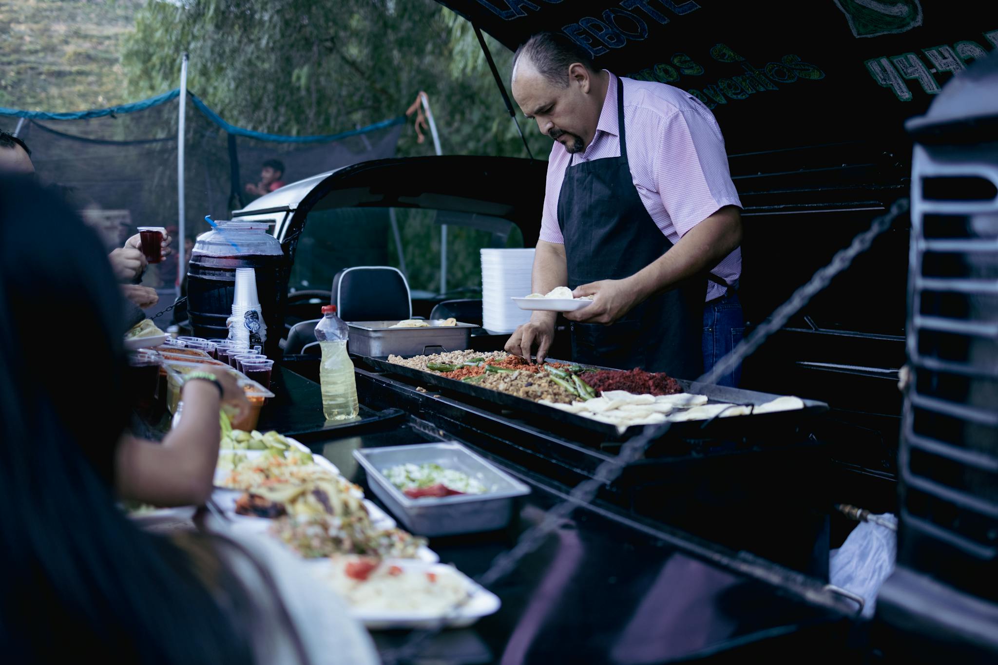 A street food vendor in San Luis Potosi prepares and serves tacos to customers at an outdoor market.