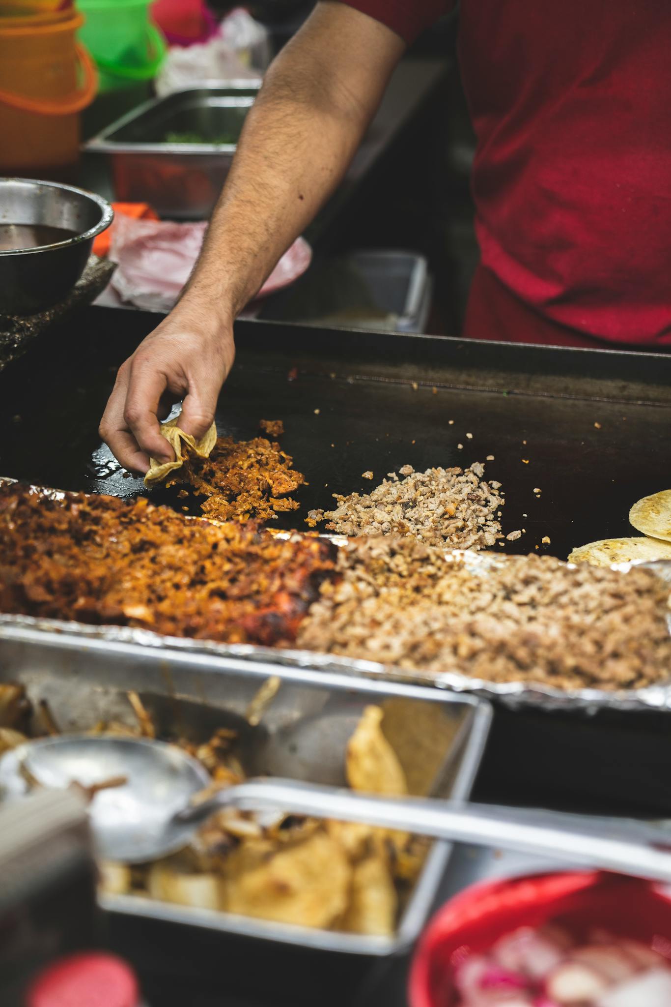 Close-up of authentic Mexican street food being prepared at a taco stand with various ingredients.