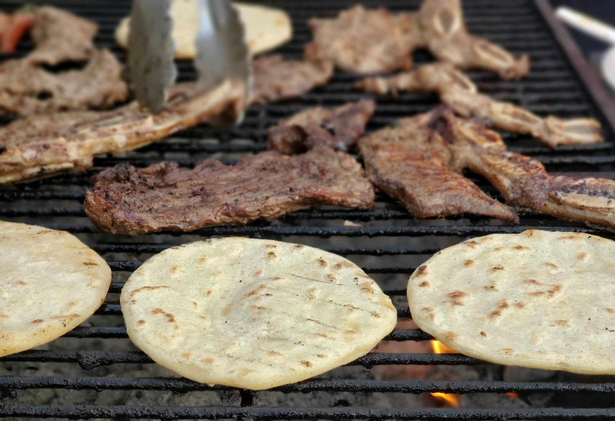 Close-up of sizzling meat and tortillas grilling on a barbecue, perfect for a delicious meal.